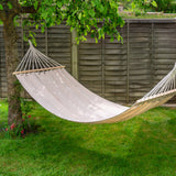Beige hammock hanging between trees in a garden with a wooden fence in the background.