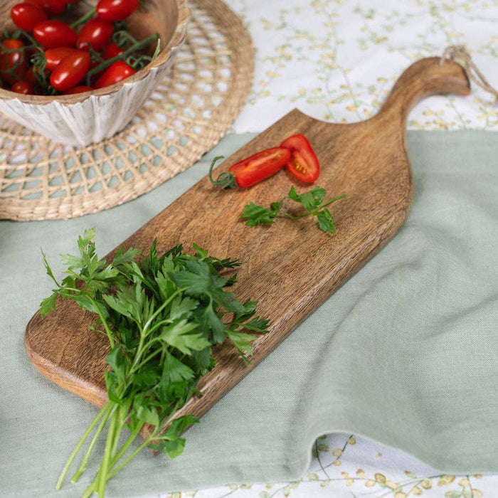 Wooden cutting board with fresh herbs and tomatoes on a light green surface.