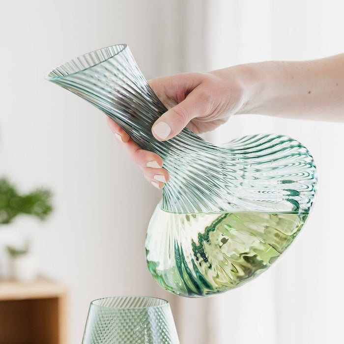 A hand holding a green ribbed glass wine decanter.