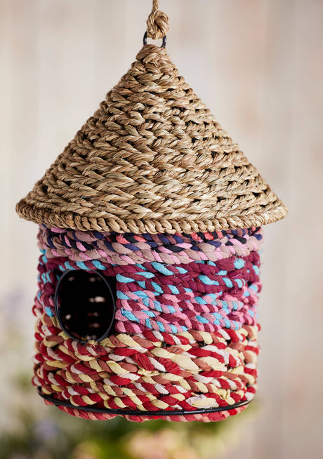 Woven birdhouse with colorful pattern and textured roof on a blurred background