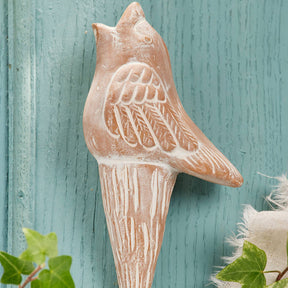 Decorative bird watering spike on a teal wooden background with greenery.