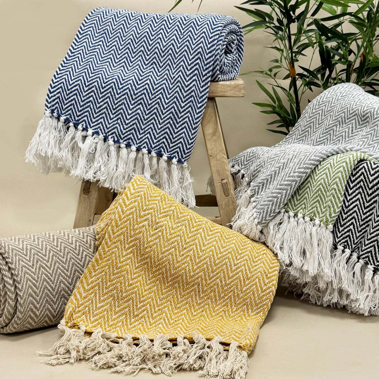 Collection of herringbone patterned throws with tassels on a wooden stool and surface.