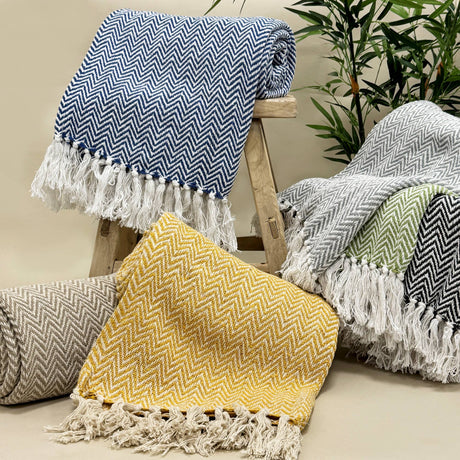 Collection of herringbone patterned throws with tassels on a wooden stool and surface.