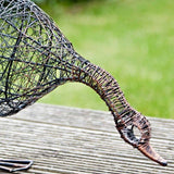 Wire sculpture of a duck drinking on a wooden surface with a blurred green background