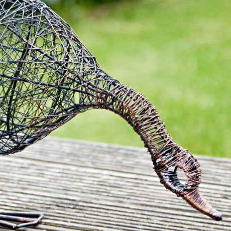 Wire sculpture of a duck drinking on a wooden surface with a blurred green background