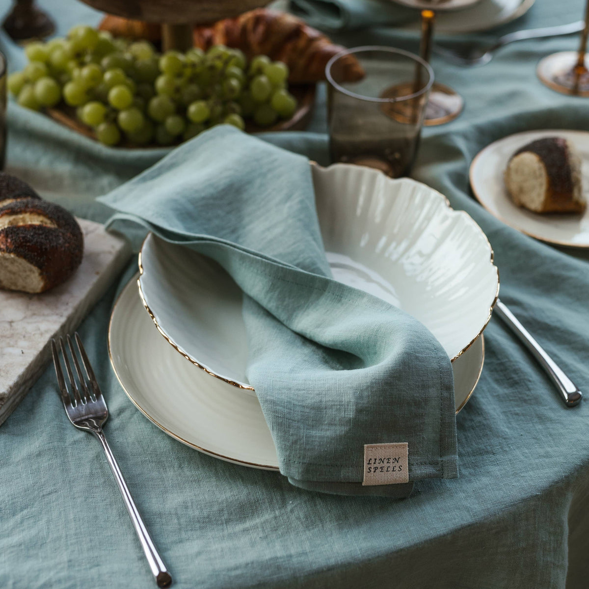 A pale blue linen napkin folded on a white plate beside cutlery and a glass.