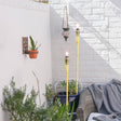 Outdoor setting with torches, plants, and a sofa against a white brick wall.