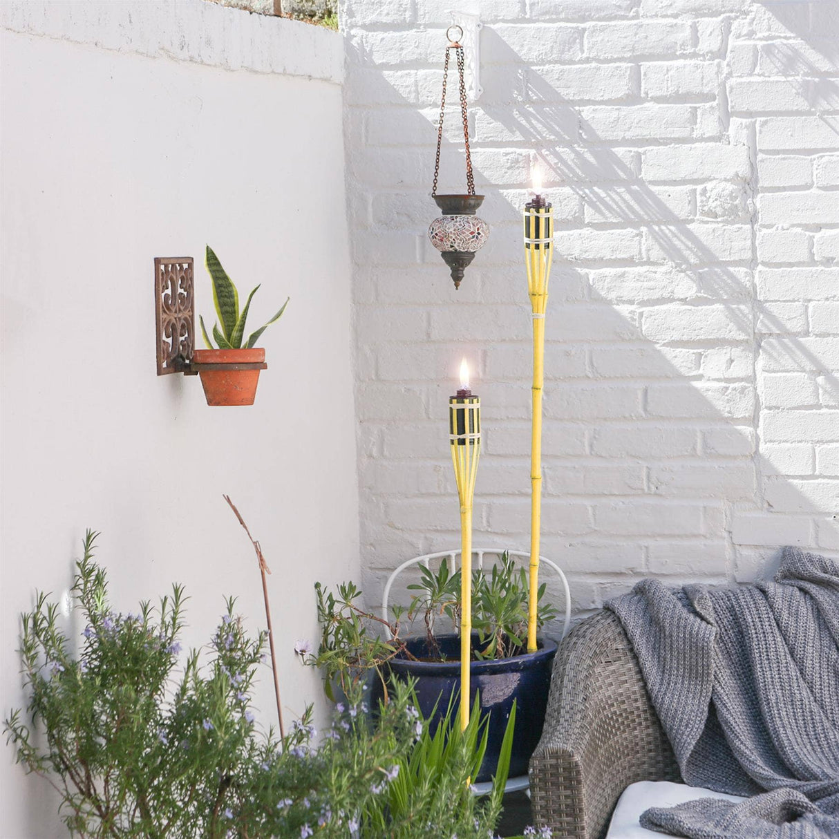 Outdoor setting with torches, plants, and a sofa against a white brick wall.