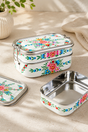 Stackable food containers with floral design on a beige surface. White Floral Garland Hand Painted Stainless Steel Tiffin Lunch Box