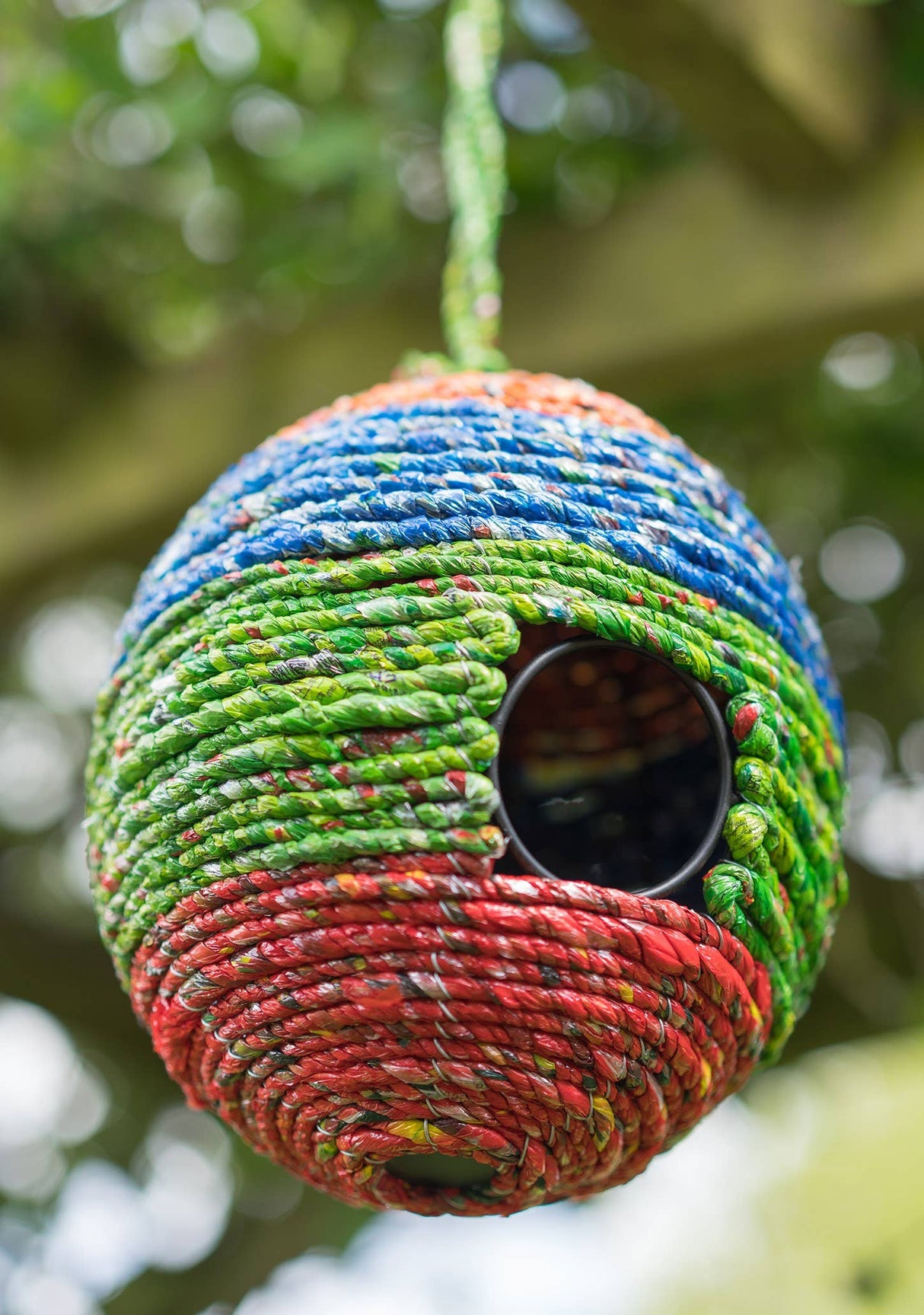 Colorful woven birdhouse hanging in a tree