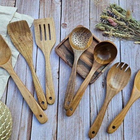 Set of wooden kitchen utensils on a wooden surface with herbs.