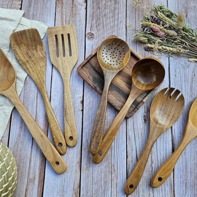 Set of wooden kitchen utensils on a wooden surface with herbs.