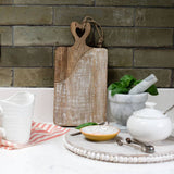 Wooden cutting board with heart handle on a kitchen counter with kitchen items.