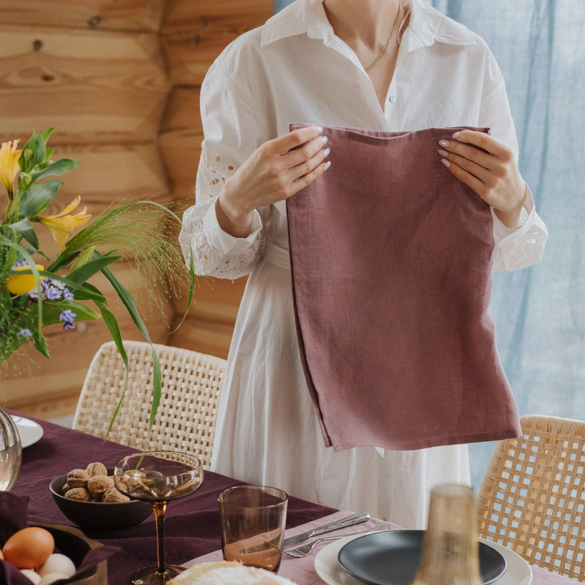 A person holding a rose-coloured linen tea towel in a light kitchen.