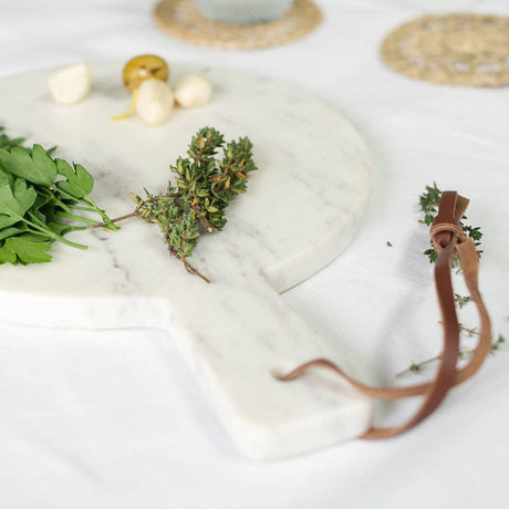 White stone surface with green herbs and a brown leather strap on a light background