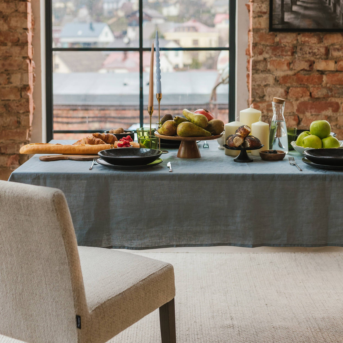 A grey linen tablecloth on a dining table beside a large window.