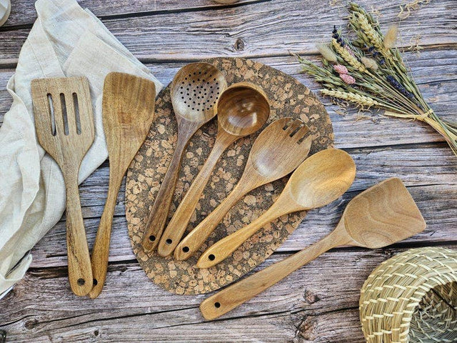 Set of wooden kitchen utensils on a rustic wooden surface with a woven mat and dried plants.