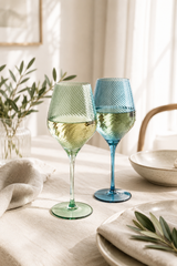 Two wine glasses, one green and one blue, on a table with a light background.