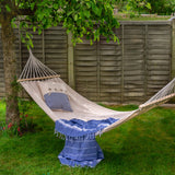 Beige hammock with blue blanket and pillow hanging in a garden