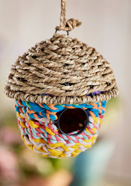 Colorful woven birdhouse with rope top on a blurred background