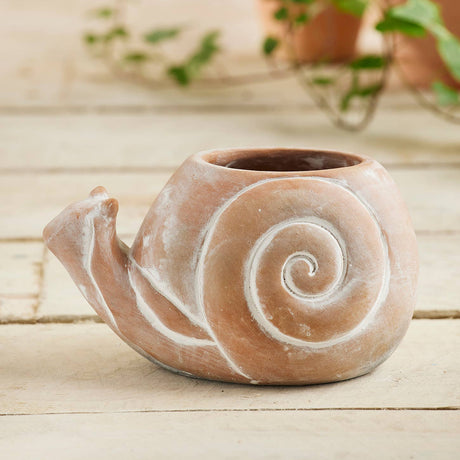 Ceramic snail-shaped planter on a wooden surface with plants in the background