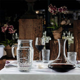 Glassware including a pitcher, wine glasses, and decanter on a table with a blurred restaurant background.