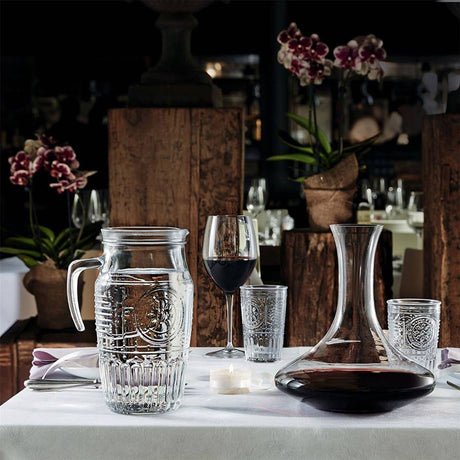 Glassware including a pitcher, wine glasses, and decanter on a table with a blurred restaurant background.