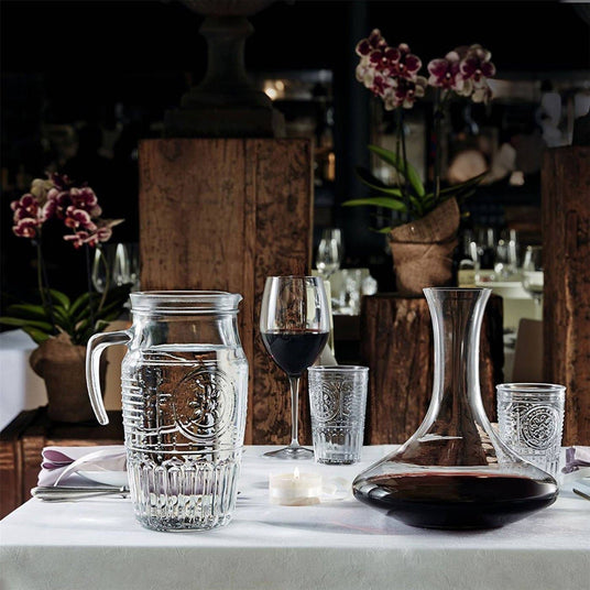 Glassware including a pitcher, wine glasses, and decanter on a table with a blurred restaurant background.