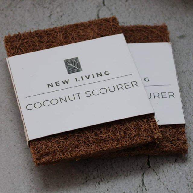 Coconut scourer and business card on a concrete surface with a textured fabric and ceramic dish in the background.