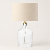 Table lamp with clear glass base and beige lampshade on a white background