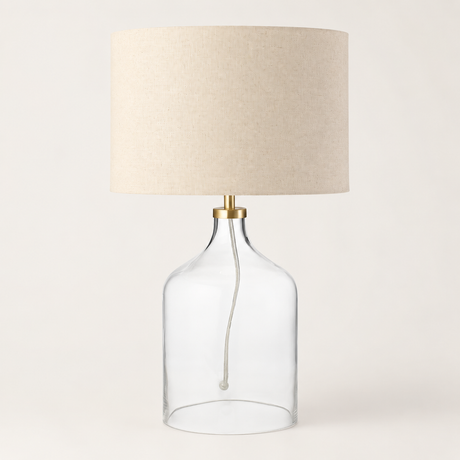 Table lamp with clear glass base and beige lampshade on a white background