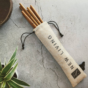 Set of bamboo straws in a beige carrying case on a concrete surface with a plant in the corner.