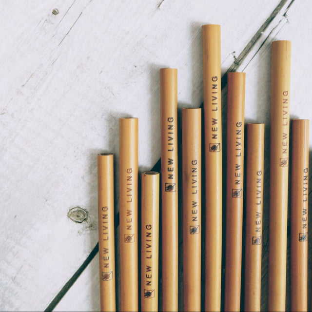 Bamboo straws with 'New Living' branding on a light wooden surface