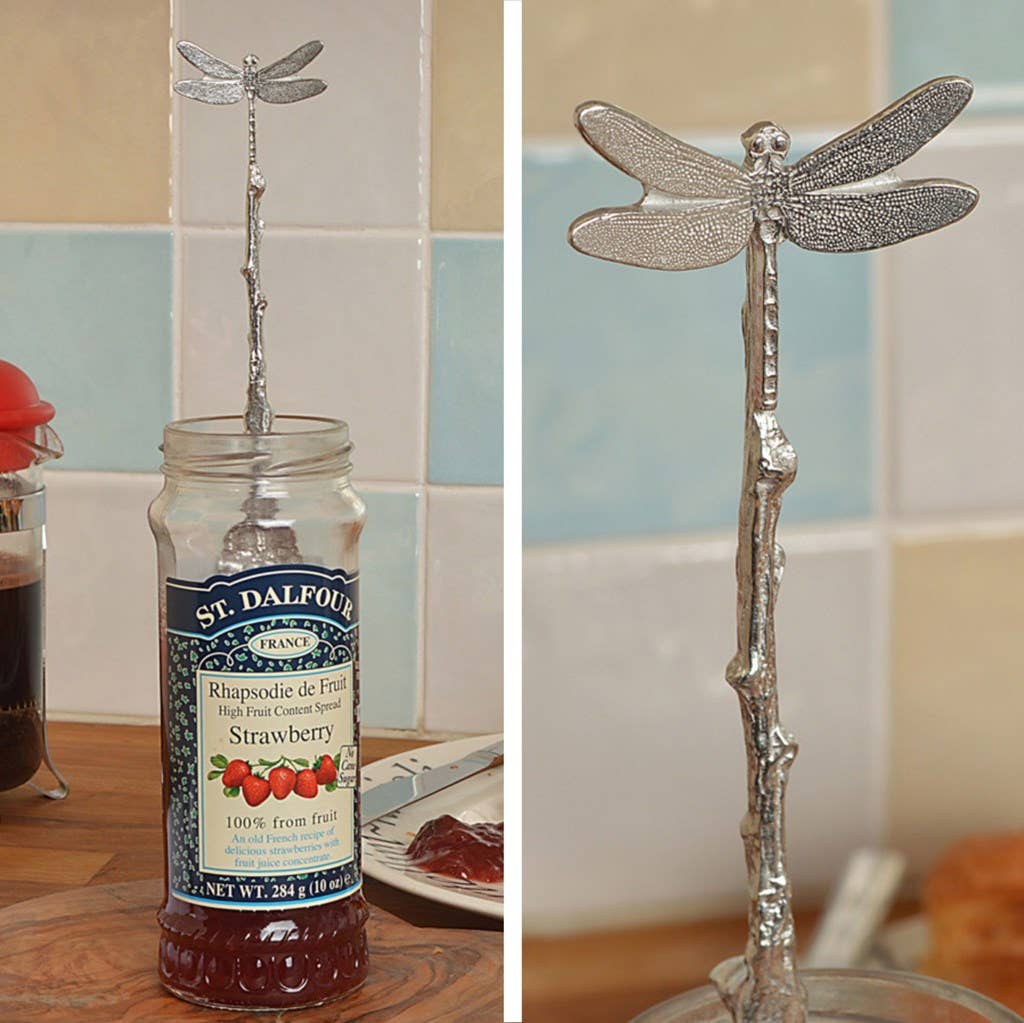Silver dragonfly-shaped spoon in a St. Dalfour strawberry jam jar with a blurred background.