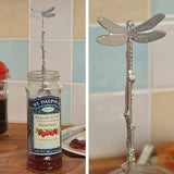 Silver dragonfly-shaped spoon in a St. Dalfour strawberry jam jar with a blurred background.