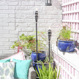 Outdoor patio with potted plants, torches, and colorful cushions against a white brick wall.