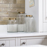 Three glass jars with gold lids on a kitchen counter with tiled backsplash