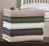 Stack of folded textured blankets in various colors on a wooden surface.