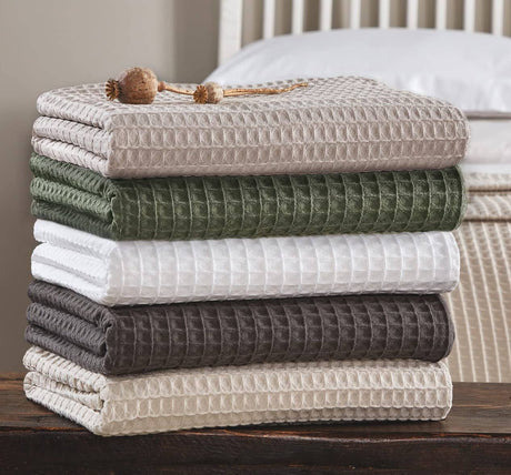 Stack of folded textured blankets in various colors on a wooden surface.