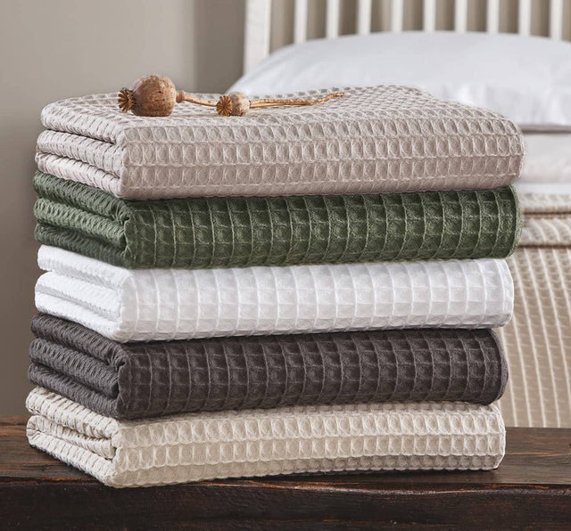 Stack of folded textured blankets in various colors on a wooden surface.