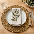Round woven placemat on a wooden surface with a table setting.