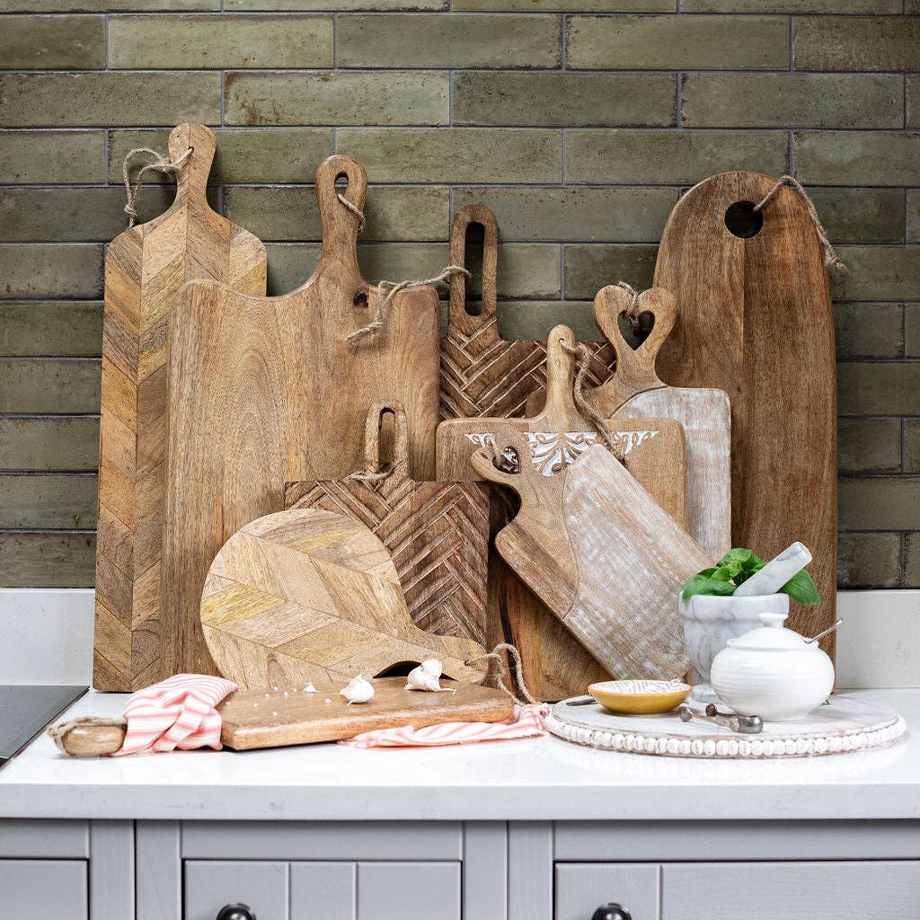 A collection of wooden serving boards in different shapes against a tiled kitchen wall.