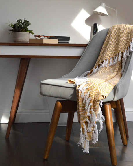Grey chair with a yellow blanket draped over it next to a wooden desk.