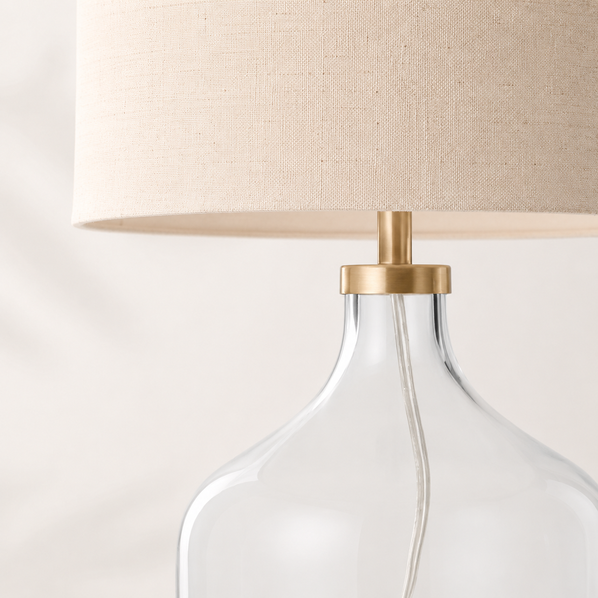 Table lamp with clear glass base and beige fabric shade on a white background