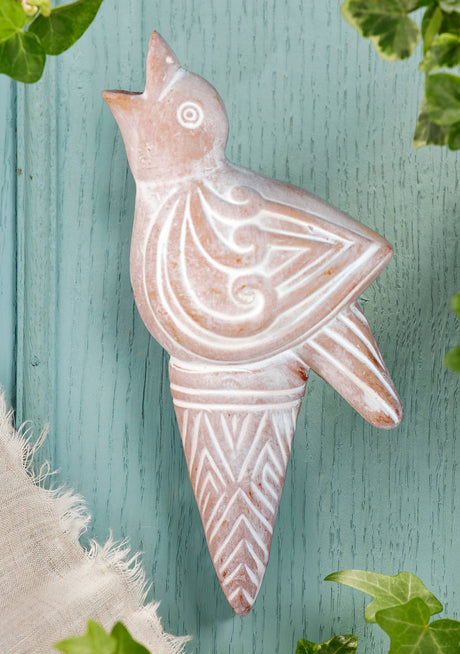 Decorative stone bird sculpture on a textured green surface with leaves around