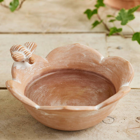 Terracotta bird bath with a snail design on a wooden surface