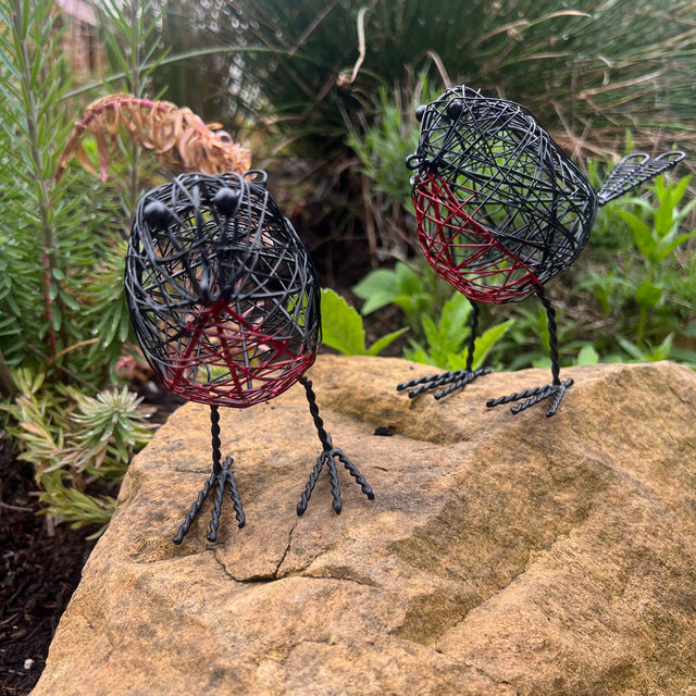 A pair of decorative wire Robbins on a rock with greenery