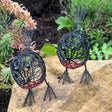 Pair of decorative wire robin birds on a rock with plants in the background