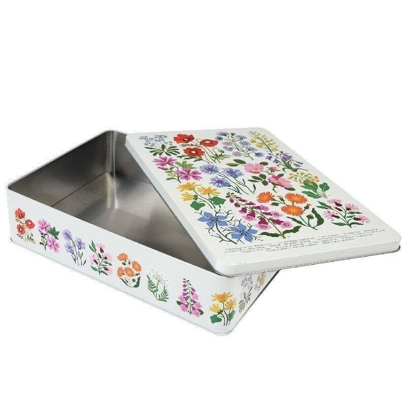 A rectangle metal tin with a lid, decorated with colourful wildflower illustrations on a white background. The interior of the tin is metallic silver, and the lid features a dense pattern of flowers in pink, orange, blue, purple, yellow, and green.