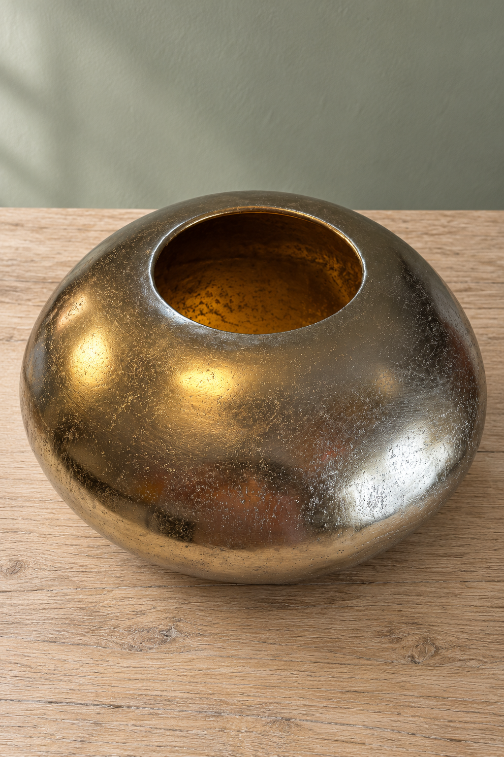 Raised view of the gold pebble bowl showing its small circular opening, gold-toned interior and mottled metal surface